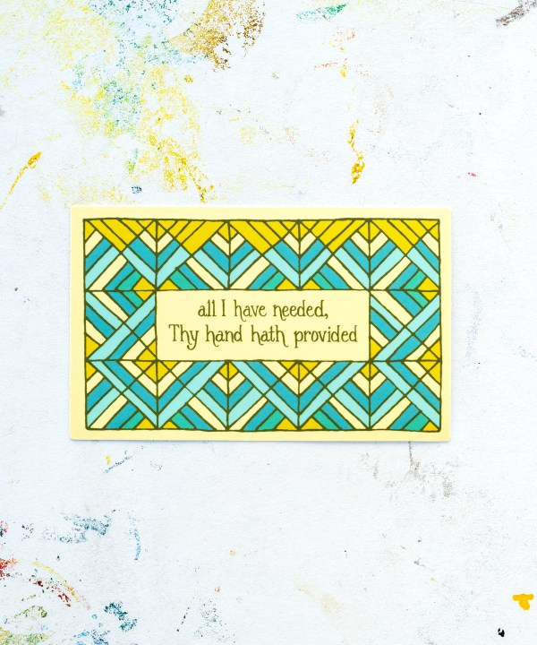 “All I Have Needed” hymn sticker features hand lettered text from "Great is Thy Faithfulness" offset by geometrical design in hues of blue, cream, and chartreuse; displayed against a white worktable background.