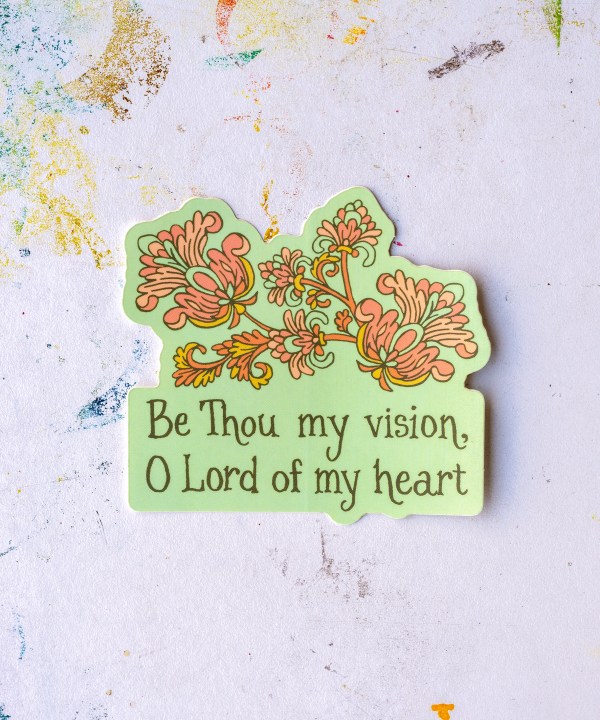 "Be Thou My Vision" hymn sticker has an aqua background with a coral and antique yellow motif. Shown against a paint-spattered worktable.