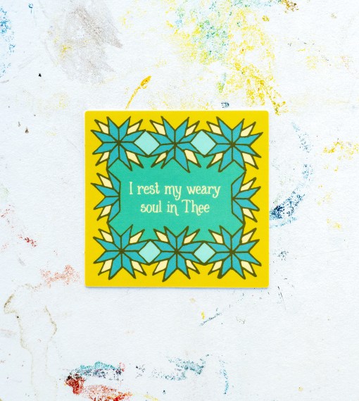 The “Rest My Weary Soul” hymn sticker features text from the hymn "O Love that Will Not Let Me Go" surrounded by a blue and cream geometrical floral design, shown against a white worktable background.