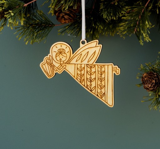 These high-flying, harp-playing angel Christmas ornaments by Little Things Studio are shining in floral motif dresses Laser cut in-house using bright maple plywood made from trees grown in North Carolina. Shown hanging with ribbon from a pine tree.