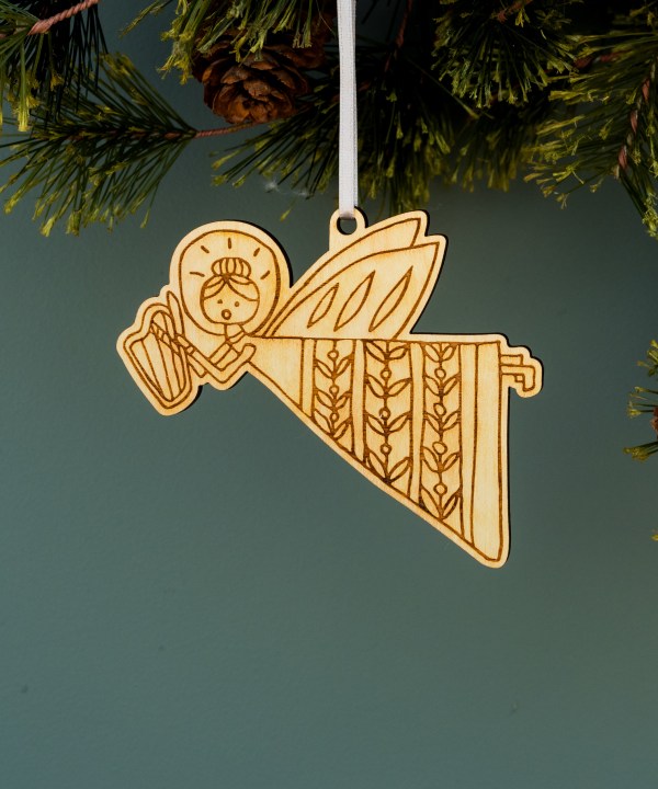 These high-flying, harp-playing angel Christmas ornaments by Little Things Studio are shining in floral motif dresses Laser cut in-house using bright maple plywood made from trees grown in North Carolina. Shown hanging with ribbon from a pine tree.