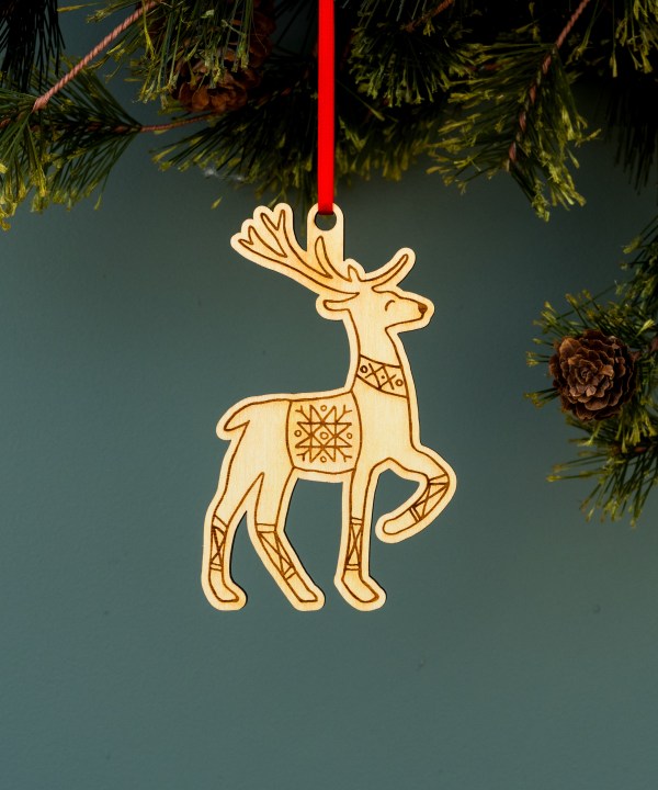 These playful prancing reindeer Christmas ornaments by Little Things Studio add a touch of whimsy and cheer to your holiday decor. Laser cut in-house using bright maple plywood made from trees grown in North Carolina. Shown here hanging from a pine tree with ribbon.